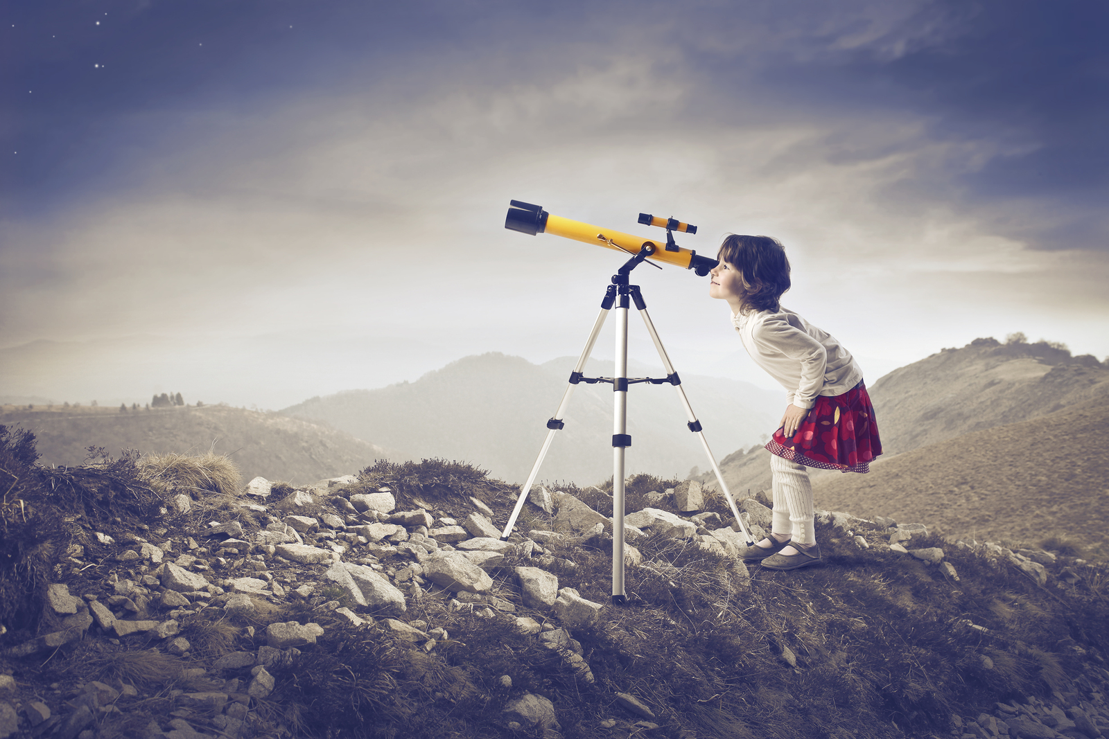 Little girl looking into a telescope in the mountains